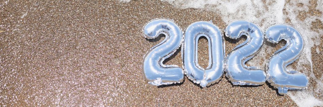 Top view of foil numbers on wet sand and foam wave on beach. Copy space in left. Waiting for the new year and new life, meet new year on holiday. Christmas, new year concept