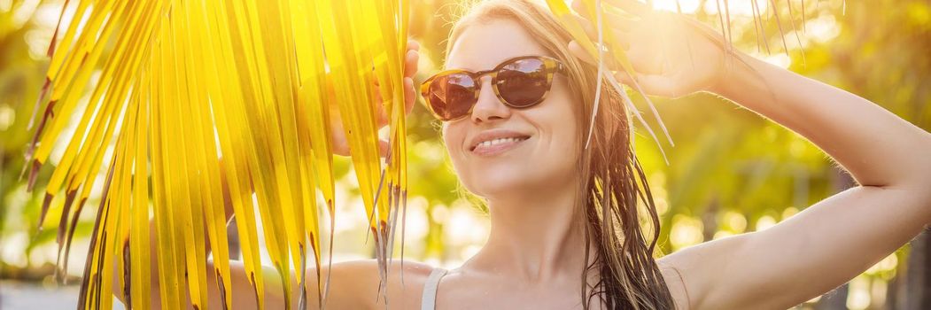 young beautiful woman in swimsuit on tropical beach, summer vacation, palm tree leaf, tanned skin, sand, smiling, happy. Happy traveller woman. BANNER, LONG FORMAT