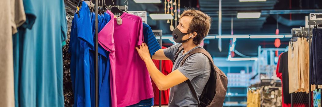 Man in a clothing store in a medical mask because of a coronovirus. Quarantine is over, now you can go to the clothing store. BANNER, LONG FORMAT