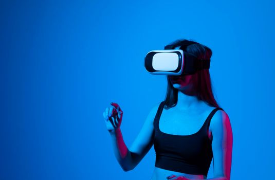 Portrait of young woman playing in VR-glasses in neon light on blue background. Concept modern gadgets and technologies. Future technology concept. Virtual reality gaming