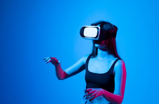 Young woman working in VR goggles on a grey background. Modern architect using virtual reality glasses at workplace. Designer working in augmented reality vr studio