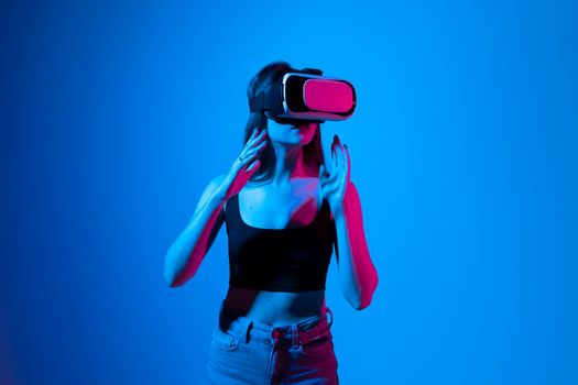 Young woman working in VR goggles on a grey background. Modern architect using virtual reality glasses at workplace. Designer working in augmented reality vr studio