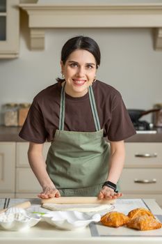 Cute young brunette smiling woman in a kitchen apron is cooking homemade baking in the kitchen.