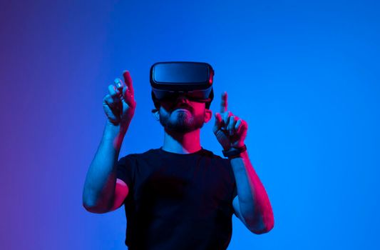 Young bearded man in virtual reality helmet plays online game in metaverse. Game simulates behavior in fictional world, gadgets and virtual reality addiction. Future technology concept