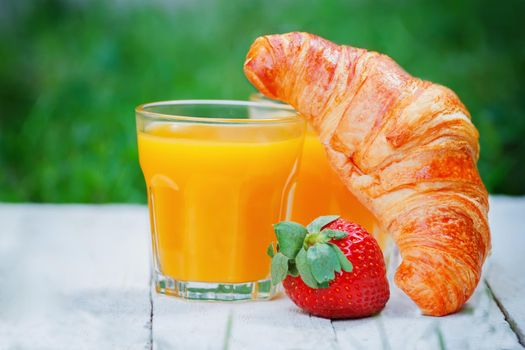 Easy breakfast outdoors with croissant, strawberry and orange juice.