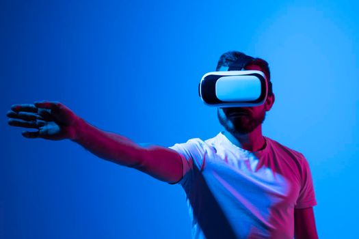 Young bearded man in virtual reality helmet plays online game in metaverse. Game simulates behavior in fictional world, gadgets and virtual reality addiction. Future technology concept