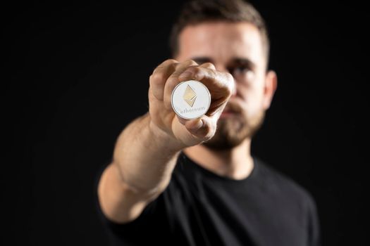 Man holds ethereum coin. Young bearded man holding virtual currency ethereum