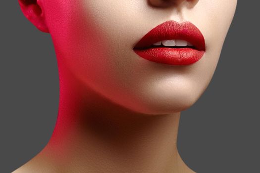 Cosmetics, makeup and trends. Bright lip gloss and lipstick on lips. Closeup of beautiful female mouth with red lip makeup. Beautiful part of female face. Perfect clean skin in red light