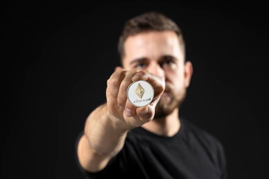 Young attractive successful bearded successful holding virtual currency ethereum coin. Cryptocurrency