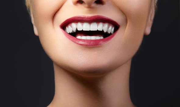 Close-up happy female smile with healthy white teeth, bright red gloss lips make-up. Cosmetology, dentistry and beauty care. Macro of woman's smiling mouth