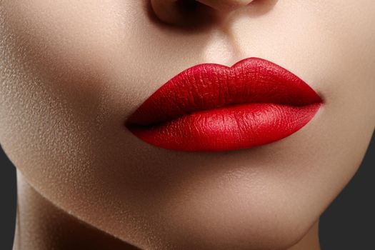 Cosmetics, makeup and trends. Bright lip gloss and lipstick on lips. Closeup of beautiful female mouth with red lip makeup. Beautiful part of female face. Perfect clean skin in red light