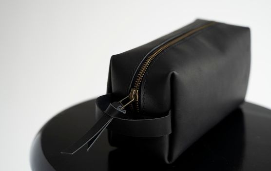 Man's black leather personal cosmetic bag or pouch for toiletry accessory on a black surface with white background. Style, retro, fashion, vintage and elegance