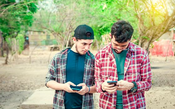 Young latin man spying on another cell phone, man showing his cell phone to another guy, two guys checking their cell phones