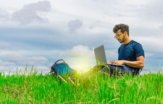 Young man in glasses working on his laptop, man in the field with his computer