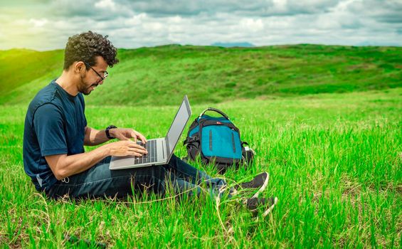 Young man in glasses working on his laptop, man in the field with his computer