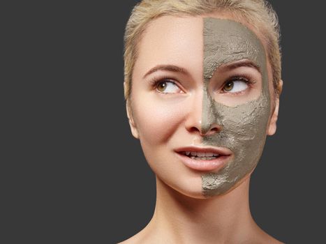 Beautiful Woman Applying Facial Mask. Beauty Treatments. Spa Girl Apply Clay Facial Mask on Grey Background. Funny Face Girl Looks at Something. Copy Space