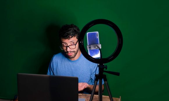Young man with laptop making video blog, Young man creator contents with celphone, man with his laptop making video call with green background,