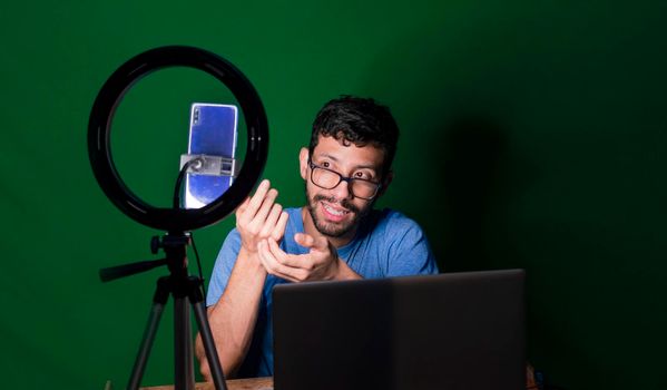 Young man with laptop making video blog, Young man creator contents with celphone, man with his laptop making video call with green background,