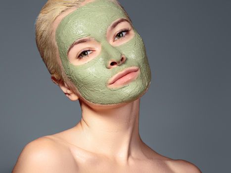 Beautiful Woman Applying Green Facial Mask. Beauty Treatments. Close-up Portrait of Spa Girl Apply Clay Facial mask on grey background