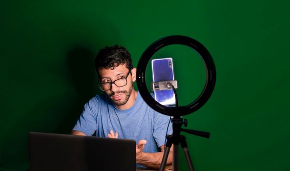 Young man with laptop making video blog, Young man creator contents with celphone, man with his laptop making video call with green background,