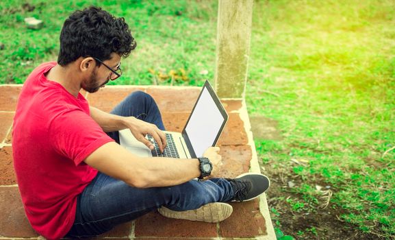 Young man in glasses working on his laptop, man on the floor with his computer