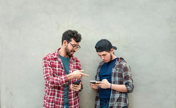 two friends transferring files from their cell phones, two guys checking their cell phones, Two young men comparing their cell phones