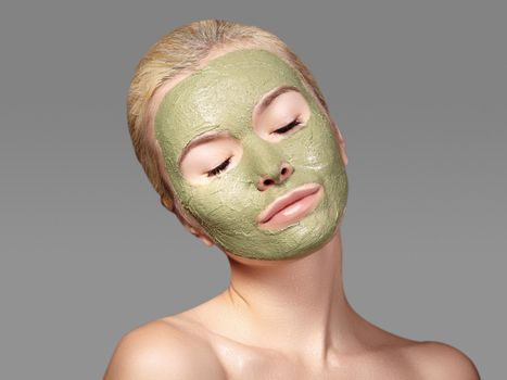 Beautiful Woman Applying Green Facial Mask. Beauty Treatments. Close-up Portrait of Spa Girl Apply Clay Facial mask on grey background