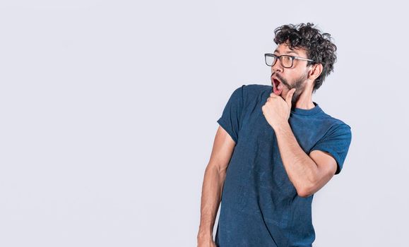 Amazed young man with hand near open mouth, man looking aside with face scared expression, surprised guy on isolated background