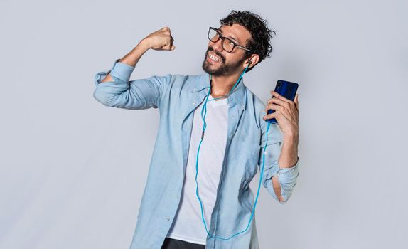 Happy man with headphones holding a cell phone and celebrates, A guy with his smartphone celebrating victory