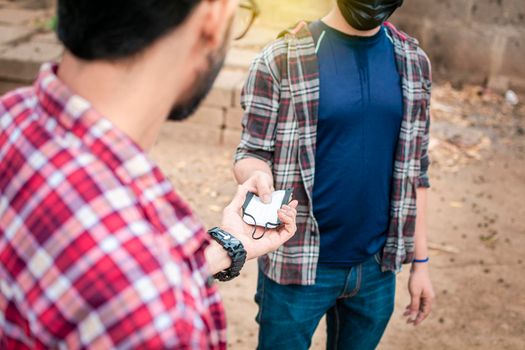 Two young people giving each other a mask, image of a young man giving a mask to another person, concept of a person offering a mask