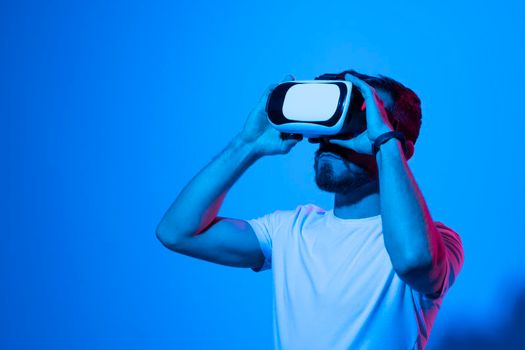 Closeup of young man wearing virtual reality goggles in modern studio with a neon light. Smartphone using with VR headset. Future technology concept