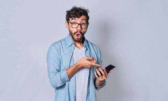 Young man showing blank cell phone screen, concept of shocked man pointing at his cell phone