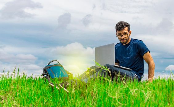 Young man in glasses working on his laptop, man in the field with his computer