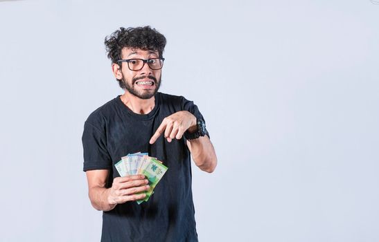 Man pointing at the money in his hand, a guy pointing at money bills in his hand, concept of earnings and savings