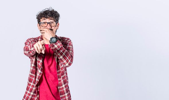 Isolated attractive guy laughing at you, young man pointing at camera with hand over mouth, male making fun of you