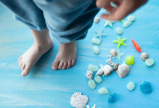 baby feet on Seashells summer background. Many different seashells, starfish on a background of blue shimmering strokes. Creative flat lay banner, workspace composition with seashell and pebbles, copy space photo. High quality photo