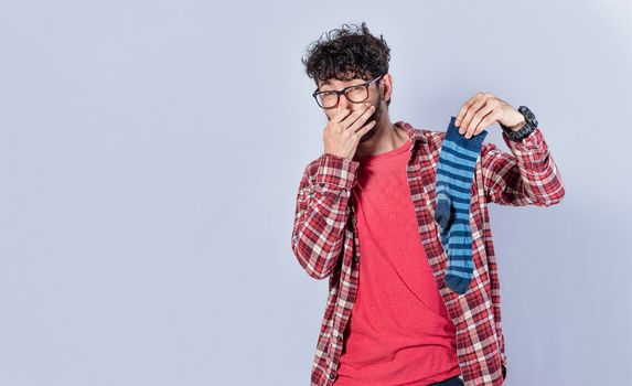 A man with a sock in his hand covering his nose, a guy with a stinky sock in his hand, smelly socks concept
