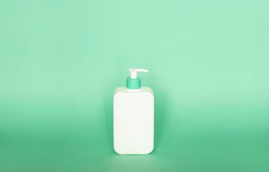 Large white plastic bottle with pump dispenser as a liquid container for gel, lotion, cream, shampoo, bath foam on green background