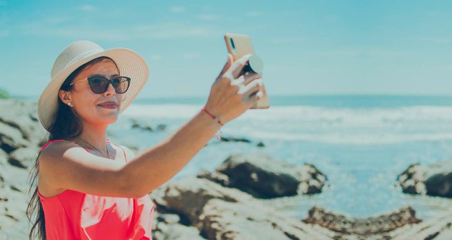 hat woman taking photos at sea, latin girl taking vacation photos, rear view of girl taking selfie on the beach