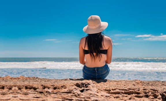 woman in hat from back to the sea, girl in hat looking to the sea, vacation concept, rear view of a girl watching the sea