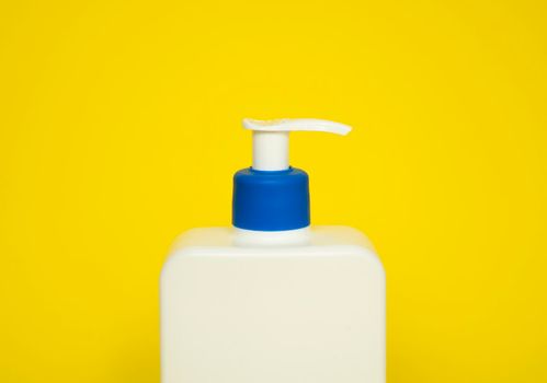 Large white plastic bottle with pump dispenser as a liquid container for gel, lotion, cream, shampoo, bath foam on yellow background