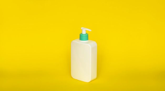 White unbranded dispenser bottle on yellow background. Cosmetic packaging mockup with copy space