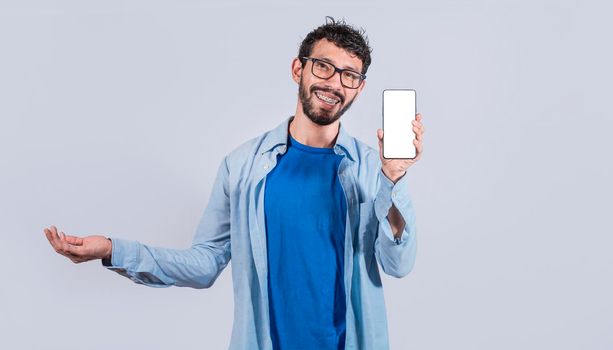 Handsome man smiling positive showing mobile phone blank screen with another hand palm open, excited happy male holding smartphone 