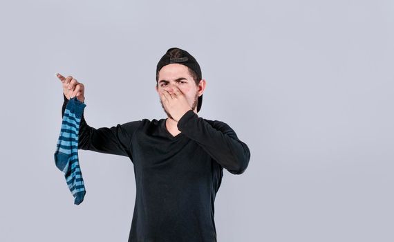 A man with a sock in his hand covering his nose, a guy with a stinky sock in his hand, smelly socks concept