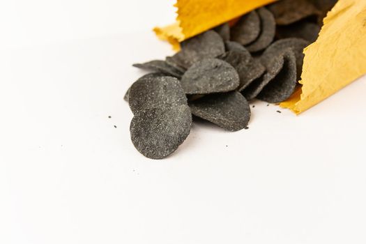 Selective focus. Macro chips in a craft bag. Spices and salt on black chips. Black chips with spices on a plate, cuttlefish ink food