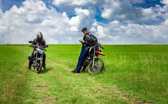Two men with their motorcycles parked chatting in the field, two young motorcyclists in the field, two men on motorcycles on a beautiful country road, young motorcyclists parked on a road