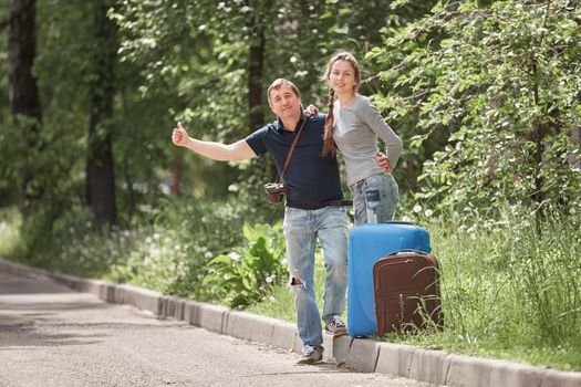 young couple with suitcases voting on the road. the concept of hitchhiking