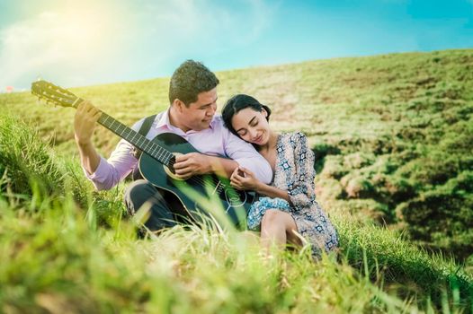 Man playing guitar to a girl, A woman leaning on the shoulder of a young man, man with woman in the field playing guitar