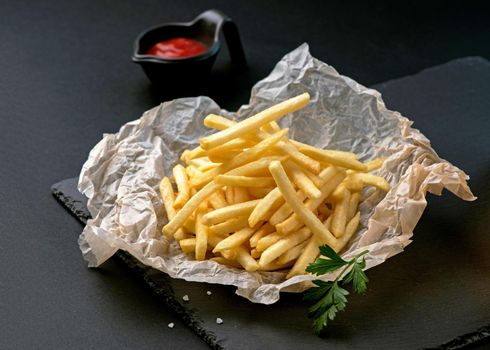 Pile of french fries placed on food oil blotting paper on black plates isolated on a black background.