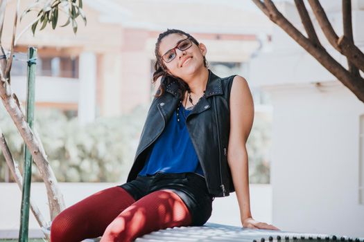 Portrait of an urban girl sitting on a bench, portrait of a latin girl on a bench looking at the camera, concept of a relaxed latin girl looking at the camera